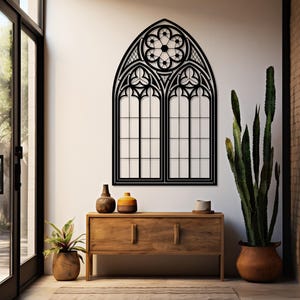 May include: Black metal gothic window wall art. The decorative piece features an arched top with a floral design and two rectangular window panels. The artwork is mounted on a white wall above a wooden cabinet with decorative items.