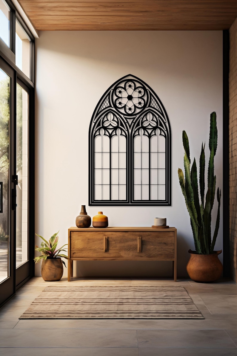May include: Black metal gothic window wall art. The decorative piece features an arched top with a floral design and two rectangular window panels. The artwork is mounted on a white wall above a wooden cabinet with decorative items.