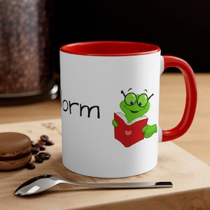 May include: White ceramic mug with a red rim and handle. The mug has a green worm with glasses reading a red book and the word "worm" printed on the front.