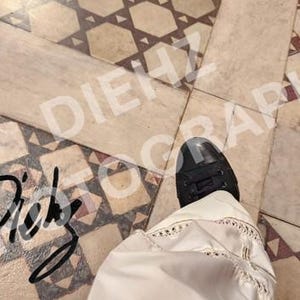 Puede incluir: Vista aérea de tres pares de zapatos de cuero negro sobre un suelo de baldosas estampadas. Un par es de estilo clásico con cordones, otro es sin cordones y el tercero es parcialmente visible. La imagen tiene un aspecto vintage.