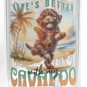 May include: Clear glass tumbler with a bamboo lid and straw. The tumbler features a colorful illustration of a brown Cavapoo dog on a beach with palm trees and the text "Life's Better with my Cavapoo."
