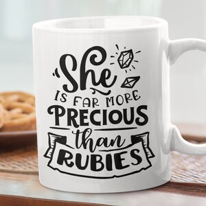 May include: White ceramic mug with a black design that reads "She is far more precious than rubies".
