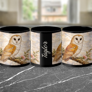 May include: Black coffee mug featuring a detailed illustration of a barn owl perched on a branch with pink flowers. The owl has white and brown feathers. The mug has the name "Taylor" printed on it.