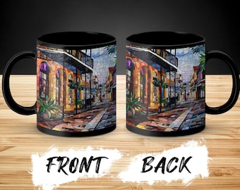May include: Black coffee mug with a colorful stained glass design of a street scene. The front of the mug shows a street with buildings on either side. The back of the mug shows the same street scene from a different angle.