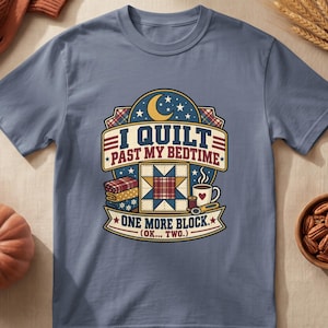 May include: A slate blue t-shirt featuring a graphic with a crescent moon, stars, and the text I QUILT PAST MY BEDTIME ONE MORE BLOCK (OK... TWO.). The design includes a quilt block, a stack of folded fabrics, a coffee mug, and sewing tools.
