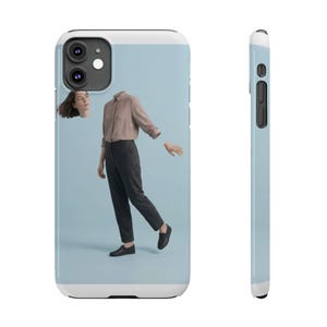 Peut inclure: Une coque de smartphone présentée sous deux angles, avec un fond bleu clair et un graphisme surréaliste composé d'une tête humaine flottante, d'un torse vêtu d'une chemise beige et d'une main détachée. Le personnage porte un pantalon gris foncé.