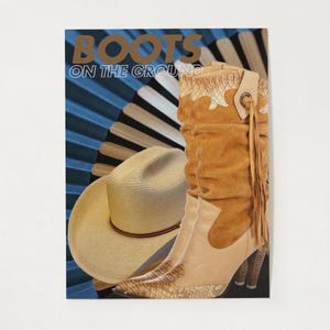 May include: A fashion-themed image featuring a cowboy hat and a high-heeled boot. The boot is tan with a snakeskin pattern on the lower part and a brown suede upper. The hat is beige with a brown band. The words "BOOTS ON THE GROUND" are at the top.