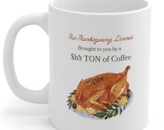 May include: White ceramic coffee mug with a brown and white illustration of a roasted turkey on a blue platter with green leaves, lemons, and raspberries. The text on the mug reads "This Thanksgiving Dinner Brought to you by a Sh!t TON of Coffee."
