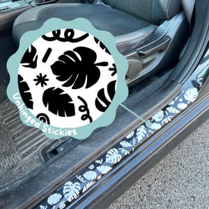 May include: Black and white car door sill protectors with a tropical leaf pattern. The pattern includes monstera leaves, swirls, and stars. The text "Unhinged Stickies" is visible on the image.