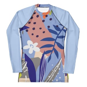 Op de afbeelding: Een shirt met lange mouwen en een lichtblauwe basiskleur met een levendig abstract patroon. Het ontwerp bevat donkerblauwe botanische bladvormen, een witte bloem met vijf bloemblaadjes en geometrische vlakken in oudroze, grijs en wit.
