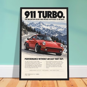 May include: A framed poster featuring a red 1987 Porsche 911 Turbo driving on a winding mountain road with snow-capped peaks in the background. The text reads 911 TURBO. THE MOUNTAIN ROAD WAS NEVER SUPPOSED TO BE EASY. PERFORMANCE WITHOUT AN EASY WAY OUT.