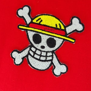 May include: Embroidered patch featuring a white skull with a yellow straw hat and crossed bones. The skull has black eyes and a black mouth. The hat has a red band.