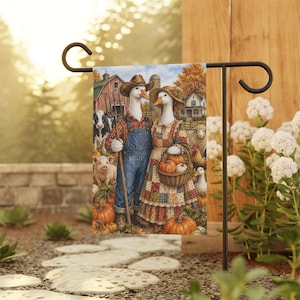 Puede incluir: Una bandera de jardín rectangular con una ilustración de dos gansos antropomórficos vestidos con ropa de granja. El ganso macho lleva un peto de mezclilla y una camisa de cuadros, sosteniendo una horca. La ganso hembra lleva un vestido de retazos y sostiene una cesta de calabazas. Animales de granja y un granero están en el fondo.
