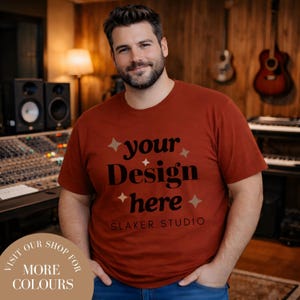 May include: A rust-colored t-shirt with the text "your Design here" in black, accented with starburst graphics. The shirt also features the text "SLAKER STUDIO". A circular graphic at the bottom says "VISIT OUR SHOP FOR MORE COLOURS".