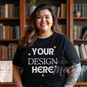 May include: A black t-shirt with the text "YOUR DESIGN HERE" in white lettering and stars. The shirt is being modelled by a person with a tattoo on their arm.