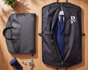 May include: A black garment bag with the name Parker printed in white, containing a blue suit jacket and white shirt. Beside it is a dark gray briefcase, a blue polka dot necktie, a silver wristwatch, and a pair of silver cufflinks.
