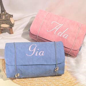 May include: Two personalized travel makeup bags, one blue with the name Gia embroidered in pink and one pink with the name Ada embroidered in white.