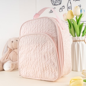 Pu&ograve; includere: Una borsa per pannolini trapuntata rosa con una tasca con cerniera e un manico superiore.