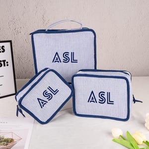 May include: Set of three blue and white striped zippered travel pouches with the initials "ASL" embroidered on each.