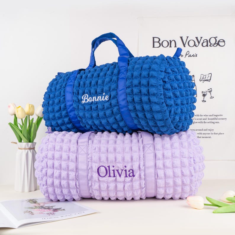 Op de afbeelding: Twee quilted reistassen, een blauwe en een paarse, met de namen "Bonnie" en "Olivia" geborduurd.