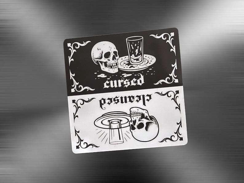 A black and white slim dishwasher magnet with a gothic theme. The top half features a skull, a dirty glass and plate, and the word 'cursed'. The bottom half shows a skull, a clean glass, and the word 'cleansed'. Ornate flourishes frame the design. Clean or dirty magnet for dishes.