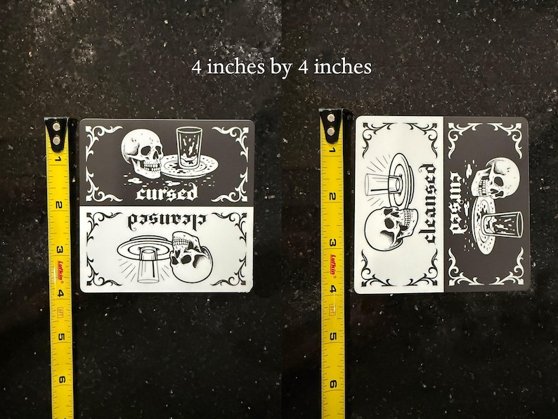 4 by 4 inch magnet. A black and white slim dishwasher magnet with a gothic theme. The top half features a skull, a glass, and the word 'cursed'. The bottom half shows a skull, a glass, and the word 'cleansed'. Ornate flourishes frame the design.