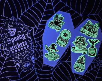 May include: A collection of spooky stickers with a Halloween theme. The stickers include coffin-shaped designs with phrases like "Crypt Coffee" and "Ouija Snacks," and a sticker sheet that says "Spooky Stickers."
