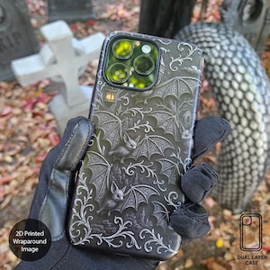 May include: Black phone case with a wraparound image featuring bats, gothic architecture, and ornate scrollwork. The case has a dual-layer design and is shown against a backdrop of fall foliage and tombstones. The case has a 2D printed wraparound image.