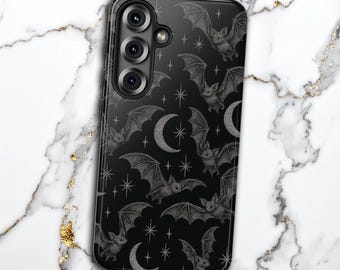 Può includere: Custodia per telefono nera con un motivo di pipistrelli, lune crescenti e stelle. I pipistrelli hanno ali dettagliate e le lune e le stelle hanno un aspetto glitterato. La custodia ha una finitura lucida e un modulo fotocamera.