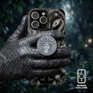 May include: Black phone case with a Medusa design and a matching phone grip. The case features a snake and floral pattern. The phone case is held by a black, textured glove. The image also shows the text "MAGSAFE DUAL LAYER".