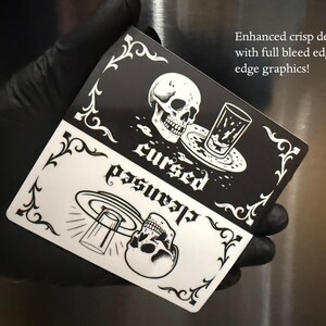 Enhanced crisp design. Full bleed graphic. A black and white slim dishwasher magnet with a gothic theme. The top half features a skull, a glass, and the word 'cursed'. The bottom half shows a skull, a glass, and the word 'cleansed'. Ornate flourishes frame the design.