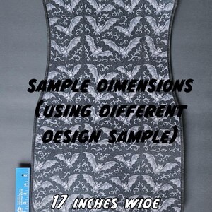 May include: A gray car floor mat with a repeating pattern of white bats and swirling designs. The mat is 17 inches wide and has the text "SAMPLE DIMENSIONS (USING DIFFERENT DESIGN SAMPLE)".
