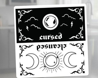 May include: A black and white magnet with the words "cursed" and "cleansed" in a gothic font. The top half features a circle with a planet design, clouds, and lightning bolts. The bottom half has crescent moons and a sun design.
