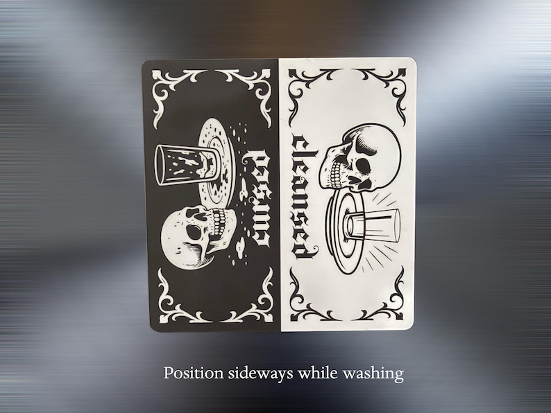 Position sideways while washing. A black and white slim dishwasher magnet with a gothic theme. The top half features a skull, a glass, and the word 'cursed'. The bottom half shows a skull, a glass, and the word 'cleansed'. Ornate flourishes frame the design.