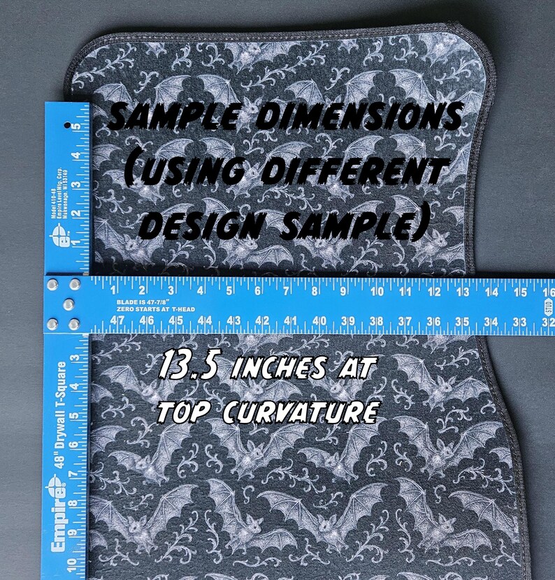 May include: A car floor mat with a bat and vine pattern in gray and white. The mat is measured with a ruler, showing a top curvature of 13.5 inches. Text on the mat reads "Sample Dimensions" and "13.5 inches at top curvature."