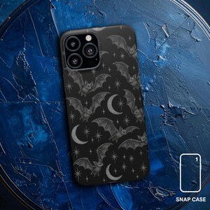 Puede incluir: Funda de teléfono negra con un patrón de murciélagos, lunas crecientes y estrellas en gris. Los murciélagos tienen alas detalladas y un estilo vintage. La funda está etiquetada como "SNAP CASE" en texto blanco.