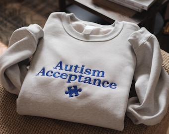 May include: A grey sweatshirt with the text "Autism Acceptance" in blue embroidery and a blue jigsaw piece.