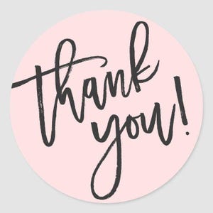 May include: Round sticker with a light pink background. The words "Thank you!" are written in a black, handwritten-style font. The design is simple and elegant, suitable for various occasions.