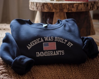 May include: A navy blue sweatshirt with the text "America was built by immigrants" and a small American flag graphic.