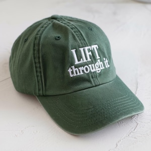 May include: A green baseball cap with white embroidery that reads "LIFT through it".