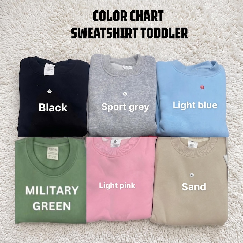 May include: A color chart for toddler sweatshirts featuring six crewneck pullovers in black, sport grey, light blue, military green, light pink, and sand. The text reads COLOR CHART SWEATSHIRT TODDLER, with labels identifying each color.