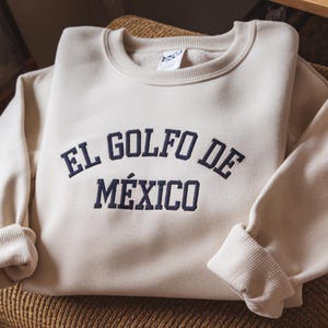 May include: A cream-colored sweatshirt with the text "EL GOLFO DE M&Eacute;XICO" embroidered in navy blue.