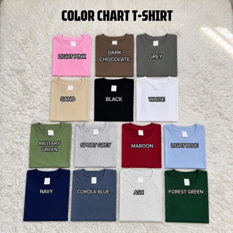 May include: A color chart t-shirt display featuring fourteen folded crew neck shirts in various colors including light pink, dark chocolate, grey, sand, black, white, military green, sport grey, maroon, light blue, navy, corola blue, ash, and forest green.