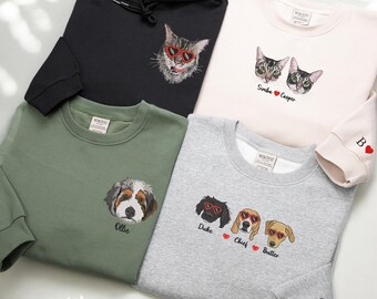 May include: A collection of sweatshirts and a hoodie featuring embroidered pet portraits. The garments are in various colors, including black, pink, green, and gray. The designs include cats and dogs wearing sunglasses, with names like Simba, Casper, Duke, Chief, and Butter.