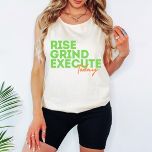 May include: Cream-colored tank top with the words "RISE GRIND EXECUTE Today" in green and orange. The top is paired with black shorts. The overall style is casual and motivational.