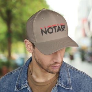 May include: A brown baseball cap with the word "NOTARY" embroidered in black letters with red accents.