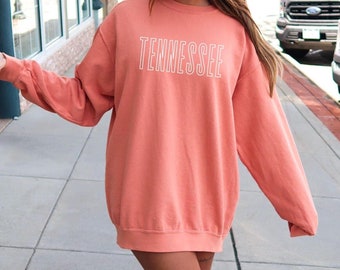 Op de afbeelding: Een koraalkleurig sweatshirt met het woord "TENNESSEE" in wit op de voorkant.
