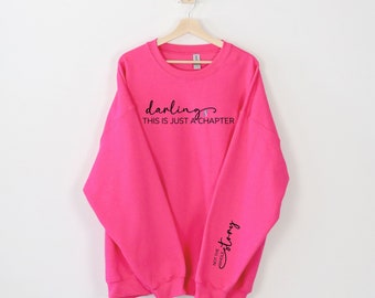 Könnte beinhalten: Rosafarbener Pullover mit dem Text "darling this is just a chapter" auf der Vorderseite und "not the whole story" auf dem Ärmel.