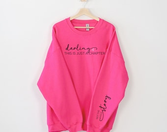 May include: A bright pink sweatshirt with the text "darling, this is just a chapter" on the front and "not the whole story" on the sleeve.
