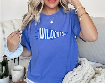May include: A blue t-shirt with a white pennant design that says "Wildcats" with a star. The shirt is made of a soft, comfortable material.